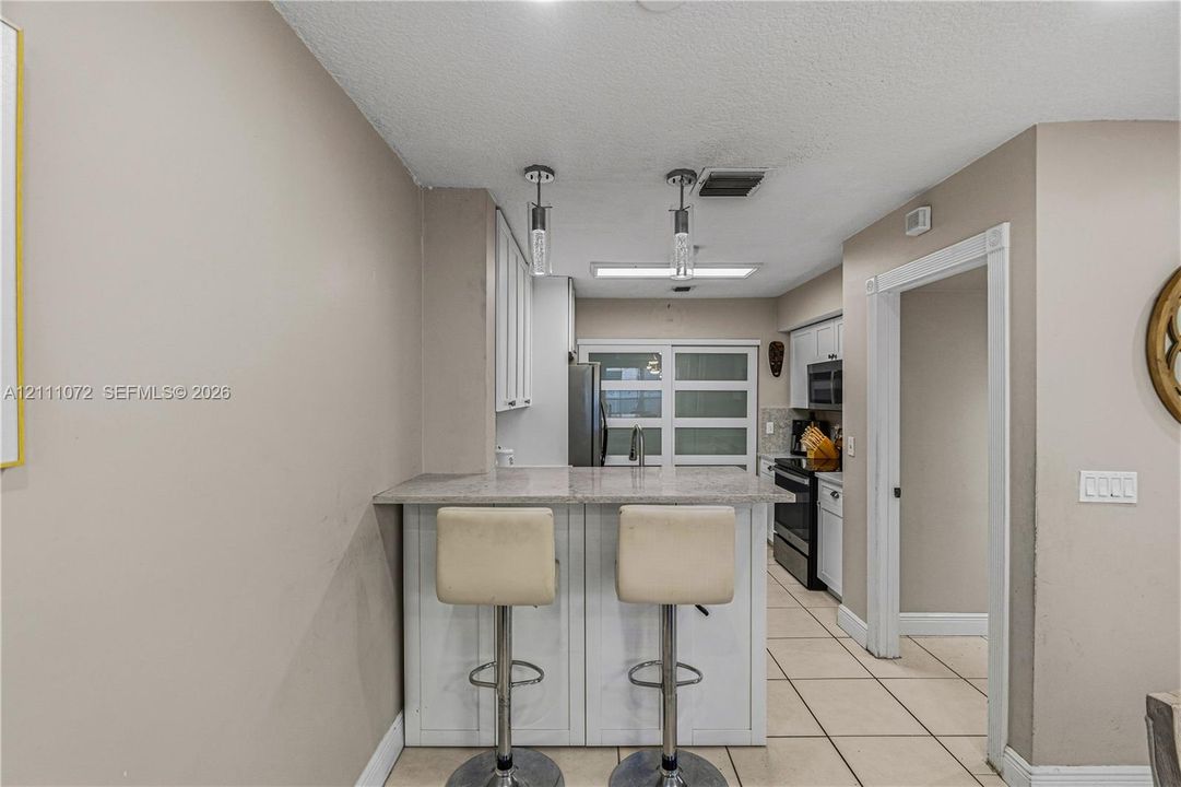 Kitchen featuring a breakfast bar with a stone-surface countertop, white cabinetry, tile flooring, and dual hanging pendant lights