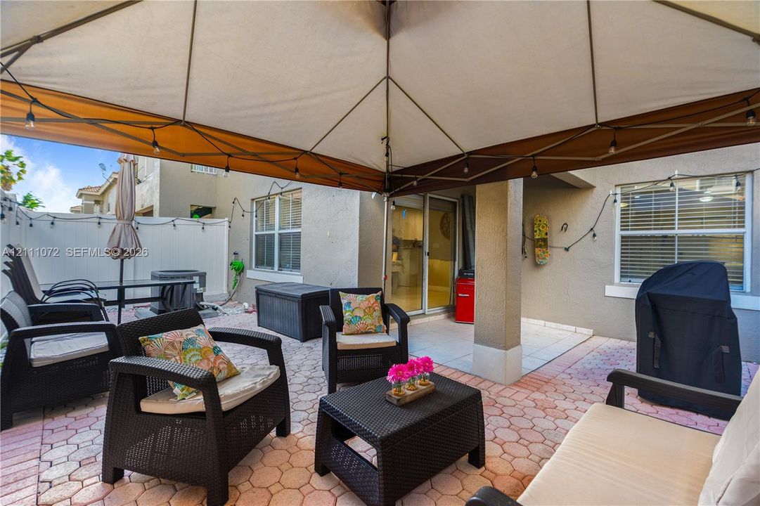 Covered patio area featuring patterned concrete pavers, neutral exterior stucco finish, and sliding glass door entry