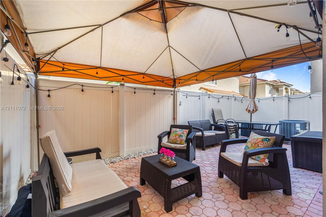 Outdoor patio featuring red-toned stone pavers, a white vinyl privacy fence, and a built-in frame structure