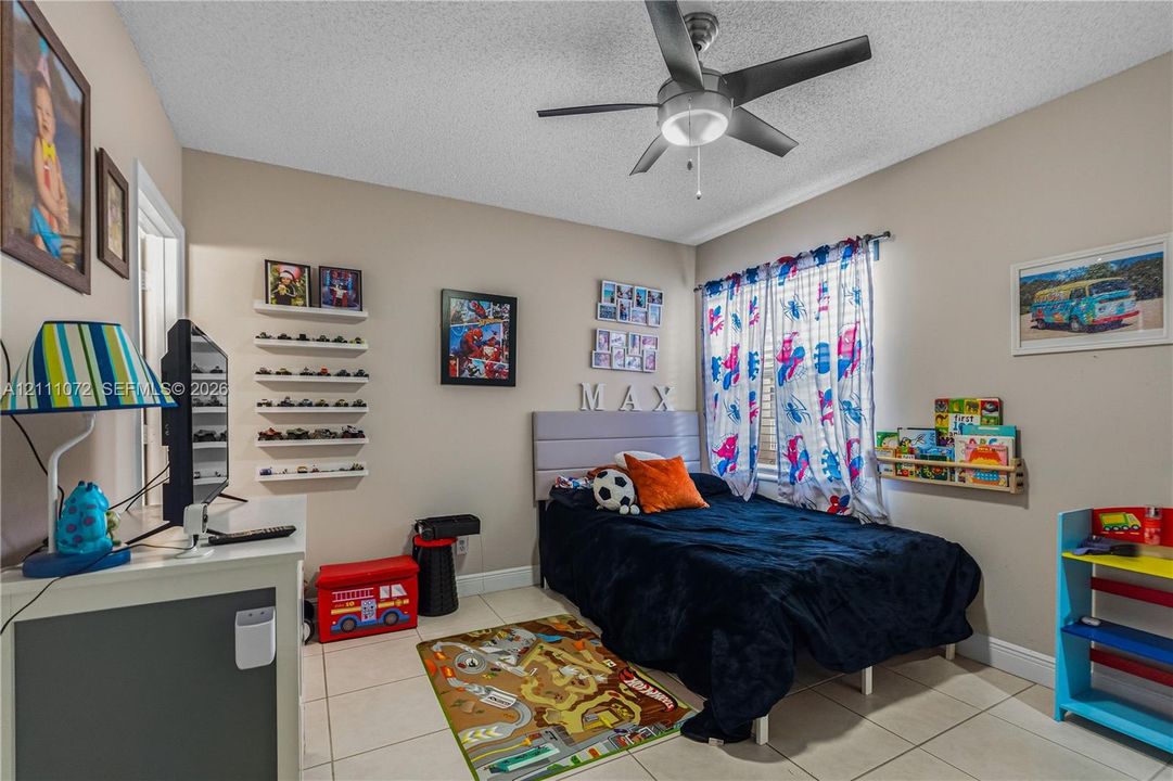 Neutral interior room featuring tile flooring, a multi-blade ceiling fan with integrated lighting, and multiple wall-mounted floating shelves