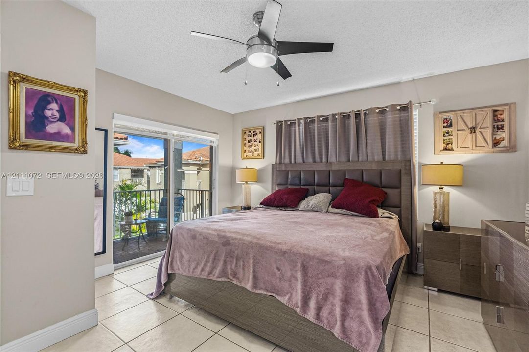 Neutral-toned interior featuring large-format tile flooring, a multi-blade ceiling fan with integrated lighting, and sliding glass doors providing outdoor access to a balcony with metal railing
