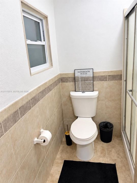 White vanity cabinet with an integrated basin, chrome-finish dual-handle faucet, wall-mounted tilting mirror, and neutral-tone tile wainscoting with decorative accent border