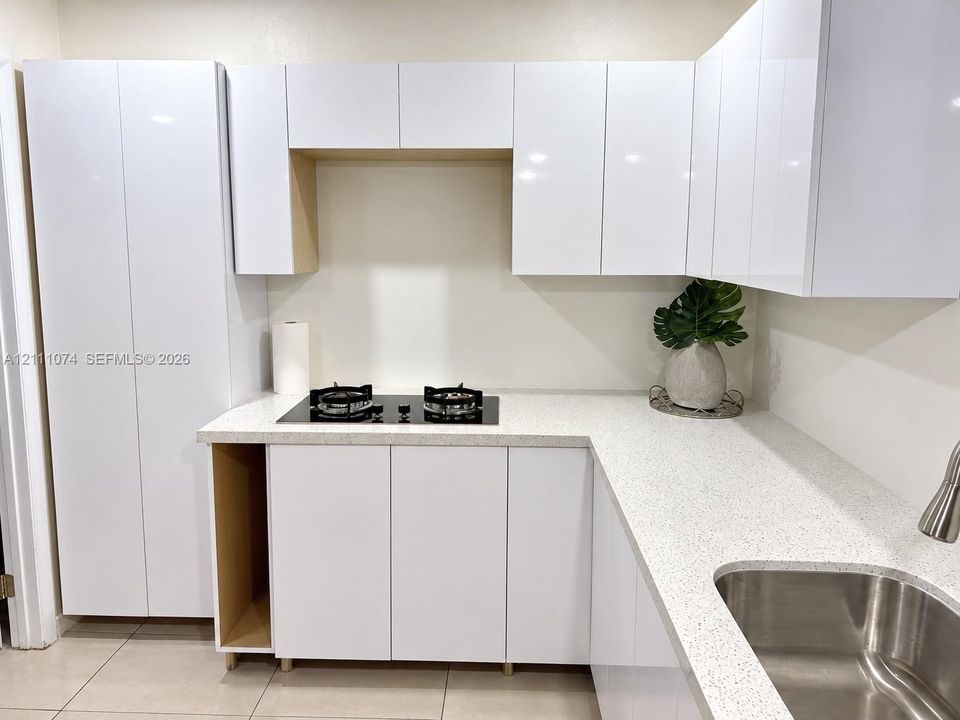 Kitchen featuring high-gloss white cabinetry, speckled quartz countertops, a dual-burner electric cooktop, and an undermount stainless steel sink