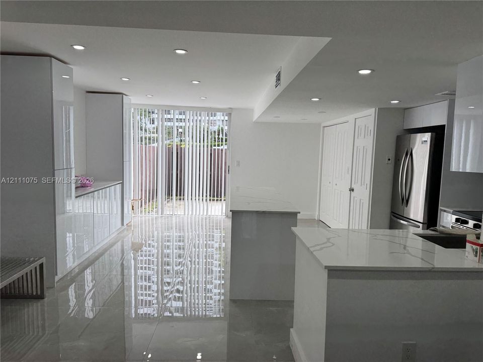 Modern kitchen featuring high-gloss cabinetry, stone-surface countertops, polished tile flooring, recessed ceiling lighting, and a stainless steel refrigerator