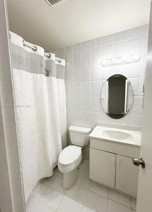 Bathroom featuring a single-sink vanity with white cabinetry, oval wall mirror, four-bulb vanity light, and tiled tub surround
