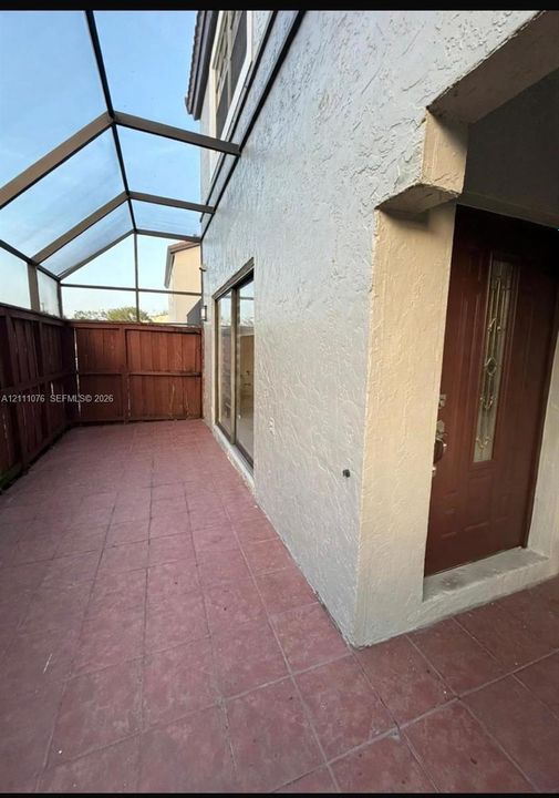 Screened-in outdoor patio featuring tiled flooring, a wood-slat privacy fence, and a decorative-glass entry door