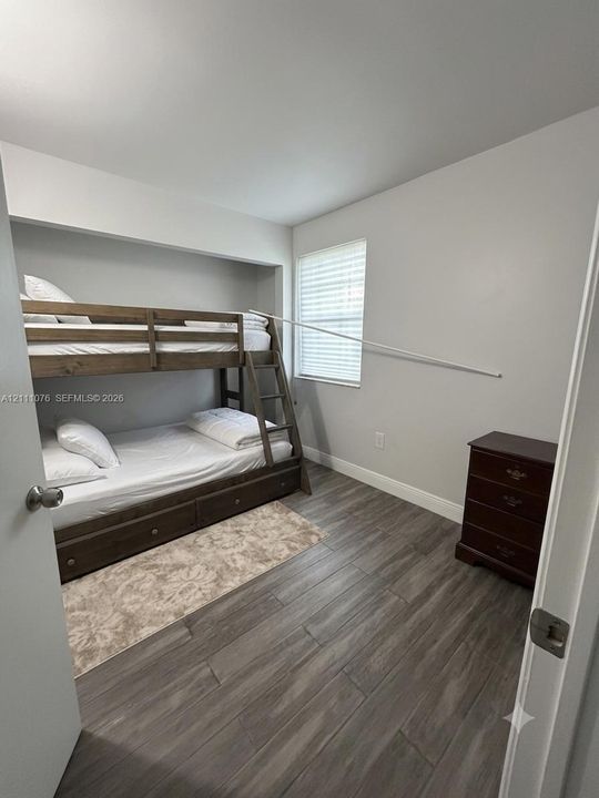 Room featuring wood-finish flooring, a recessed alcove, and a window with installed blinds