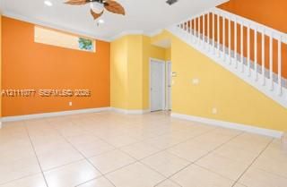 Ceramic tile flooring, white staircase with handrail and balusters, ceiling fan with light fixture, and horizontal clerestory window