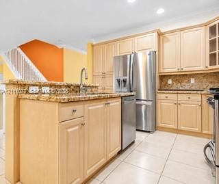 Kitchen featuring light-finish cabinetry, granite countertops, stainless steel appliances, a center island with a sink, and tile flooring