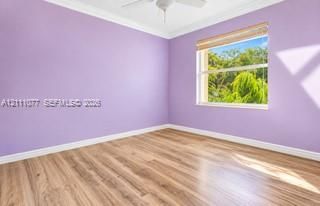 Room featuring wood-finish flooring, crown molding, a ceiling fan, and a window with wood-slat blinds overlooking exterior foliage