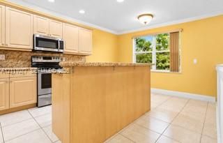 Kitchen featuring light-tone cabinetry, granite-surface countertops, stainless steel appliances, a multi-tier island, and tile flooring