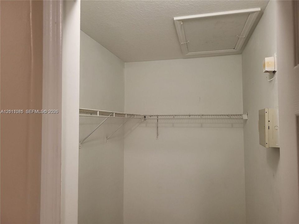 Storage closet featuring wire shelving, an attic access panel, and a mounted electrical service panel