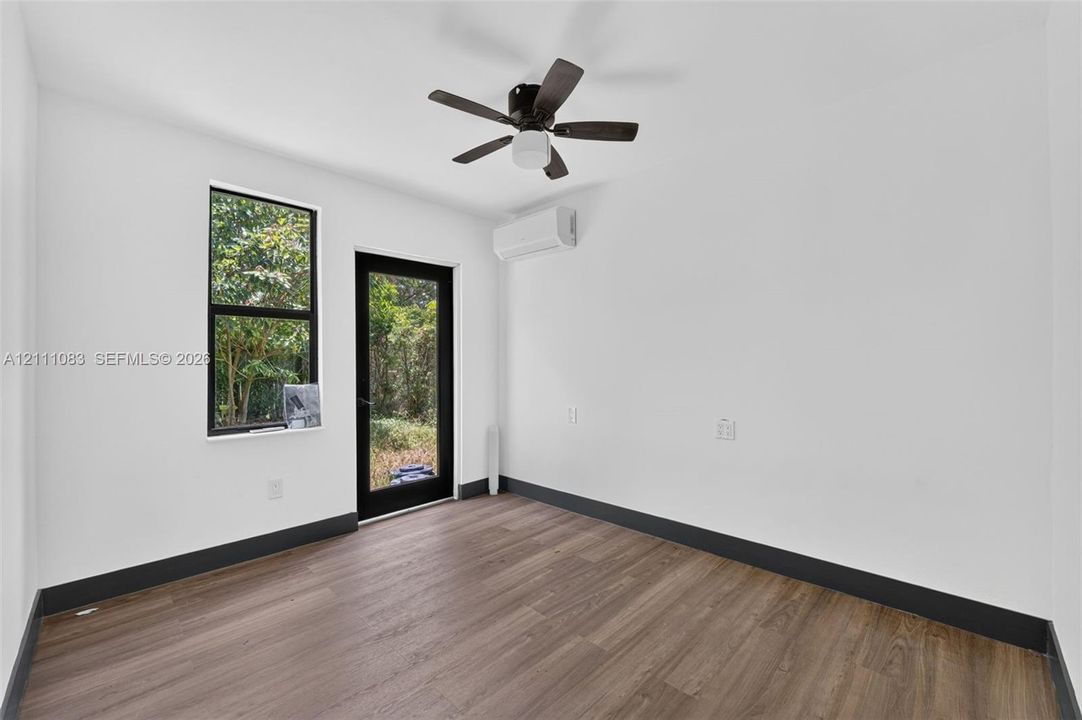 Interior room featuring wood-finish flooring, a wall-mounted ductless mini-split system, a ceiling fan with integrated lighting, and a glass-paneled exterior door