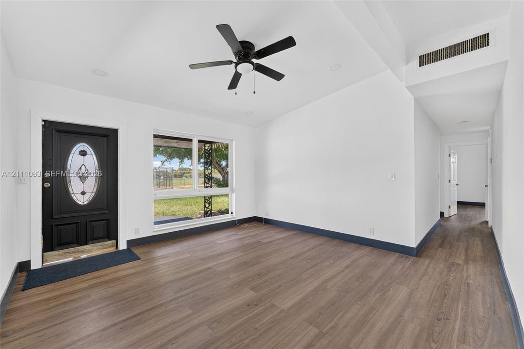 Interior featuring wood-finish flooring, vaulted ceiling, black exterior entry door with glass inlay, large window, and ceiling fan