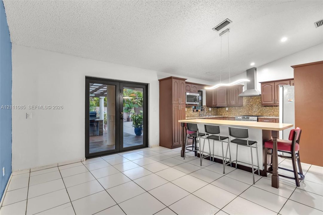Kitchen featuring brown cabinetry, stone-tiled backsplash, integrated stainless steel appliances, a breakfast bar, and double glass-paned doors with exterior access