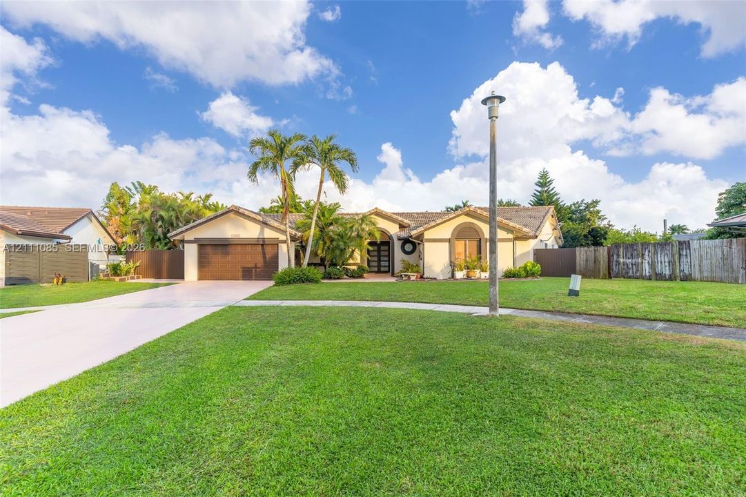 Single-story residence featuring a tile roof, light-colored stucco exterior, arched entryway, wooden garage door, and a spacious front lawn