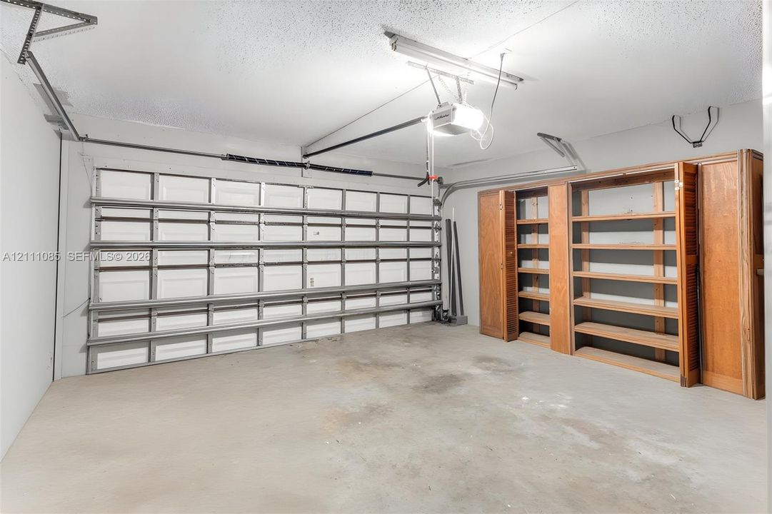 Enclosed garage featuring concrete flooring, a paneled sectional door, and built-in wood shelving units