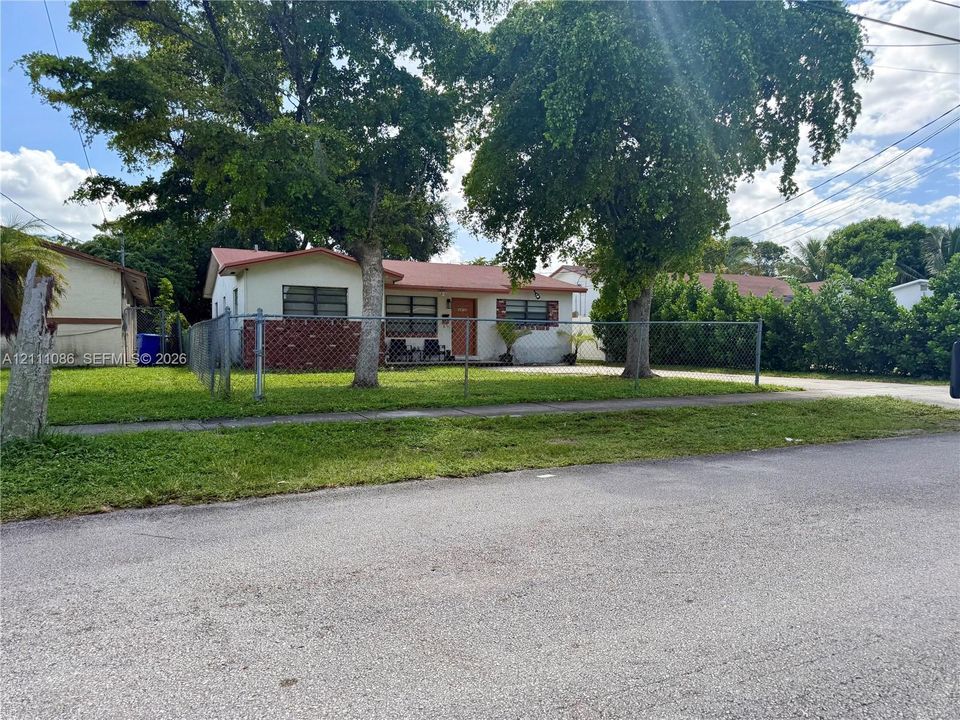 Single-story exterior featuring a metal roof, brick facade accents, mature trees, and chain-link fencing