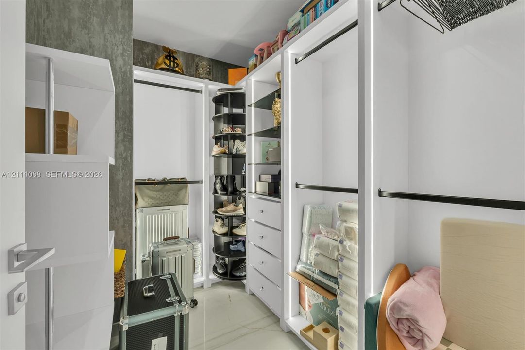 Customized storage system featuring white built-in cabinetry, integrated LED vertical lighting, a rotating shoe rack, multiple drawers, and hanging rods