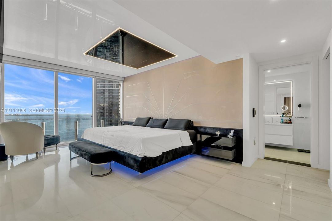 Floor-to-ceiling glass windows, recessed ceiling feature with integrated lighting, custom wall detailing, stone-finish flooring, and built-in vanity