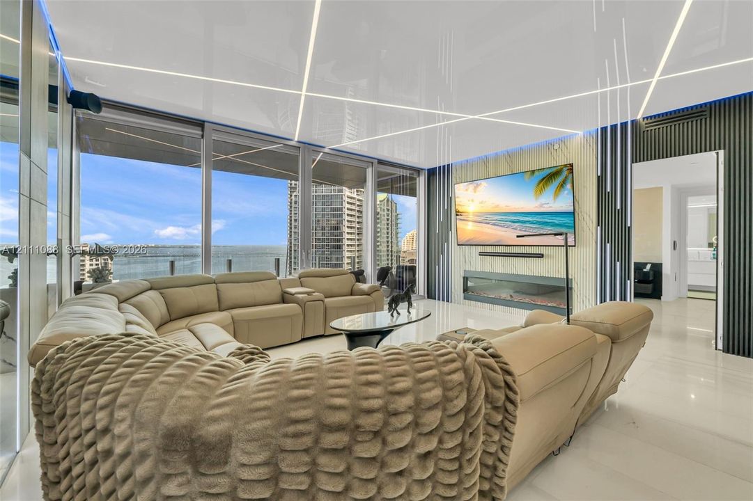 Floor-to-ceiling windows, linear recessed ceiling lighting, wall-mounted linear fireplace, textured feature wall, and polished stone flooring