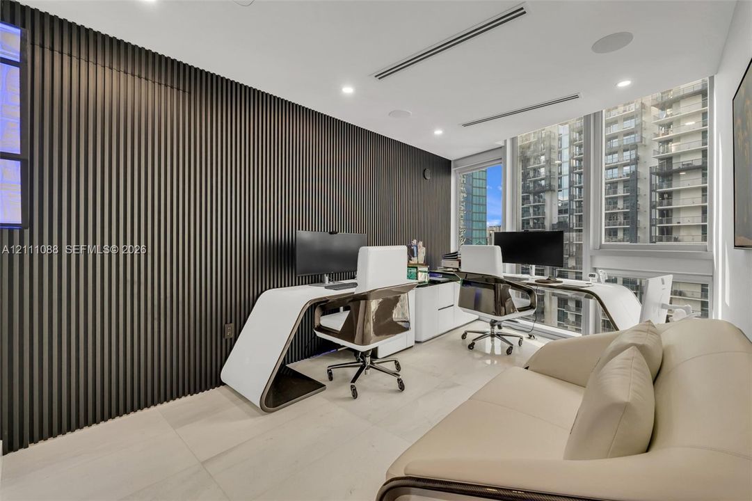 Interior space featuring a full-height, dark-toned slat wall treatment, neutral-toned large-format flooring, recessed ceiling lighting, integrated audio speakers, and expansive floor-to-ceiling windows