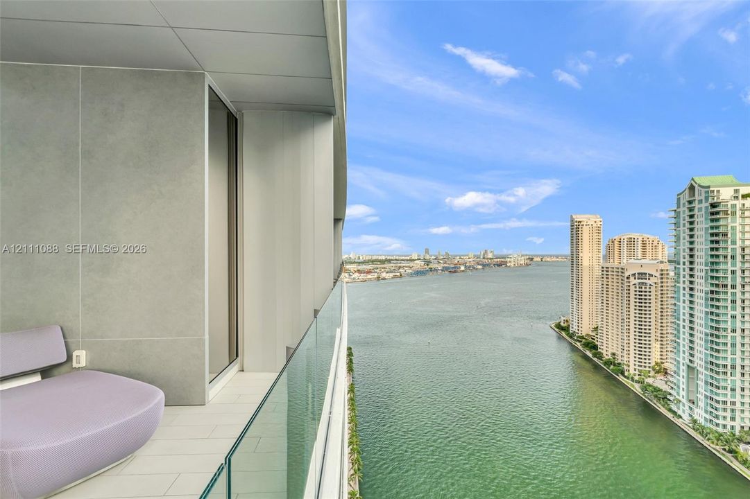 Private balcony featuring large-format tile flooring, concrete-finish wall panels, and a frameless glass railing overlooking the waterway