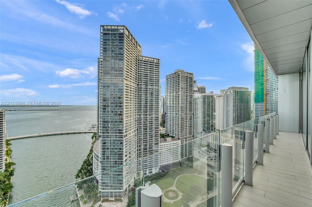 Covered outdoor balcony featuring light-toned tile flooring and transparent glass panel railings