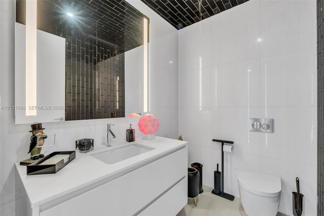 Modern floating vanity featuring a rectangular integrated sink and white stone-finish countertop, complemented by a large rectangular mirror with integrated LED lighting, wall-mounted dual-flush toilet system, and high-contrast black subway tile detailing on the ceiling and wall