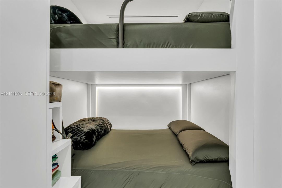 Built-in white stacked bunk structure featuring integrated shelving and recessed LED accent lighting