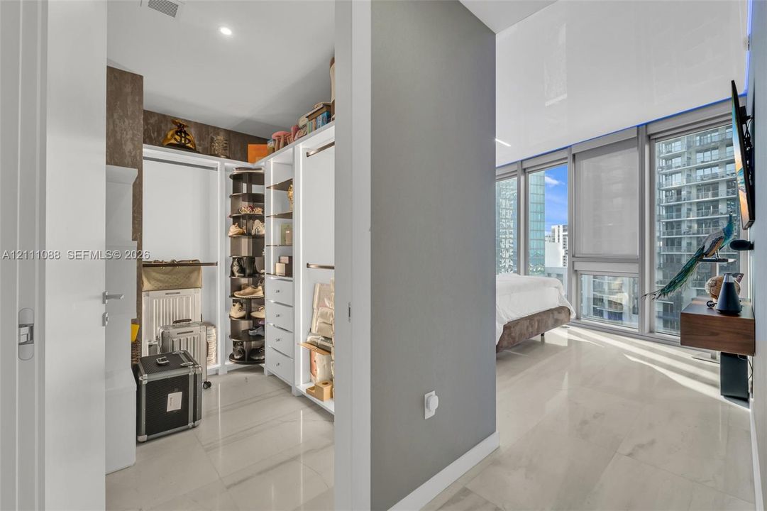 Walk-in closet featuring custom white built-in shelving, a rotating shoe rack, and stone-finish tile flooring throughout