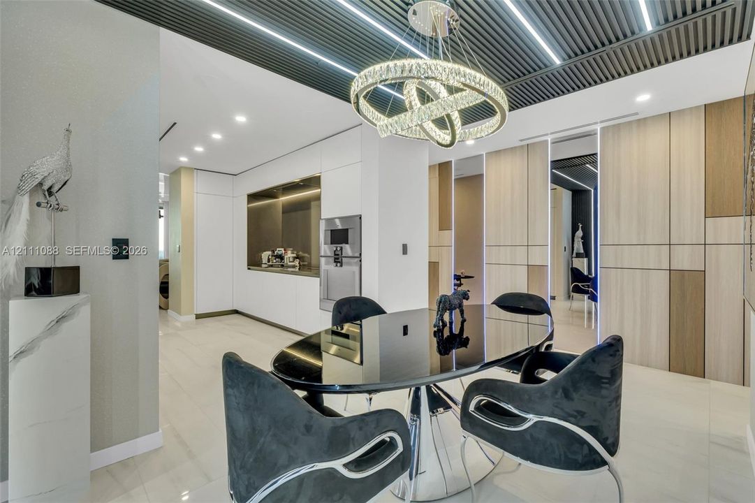 Slatted ceiling with integrated linear lighting, custom circular crystal chandelier, built-in floor-to-ceiling cabinetry with wood-finish paneling, and smooth-surface flooring