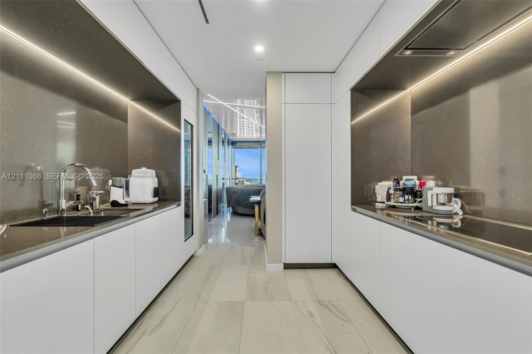 Contemporary kitchen featuring white flat-panel cabinetry, solid-surface countertops, integrated under-cabinet lighting, a built-in cooktop, and large-format tile flooring
