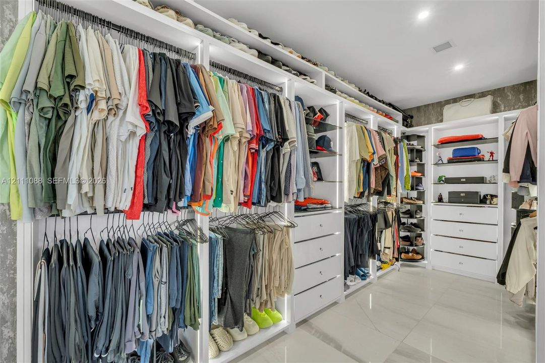 Custom walk-in closet featuring extensive white built-in cabinetry, integrated LED vertical lighting, multiple drawers, open shelving, and polished stone-finish floor tiling