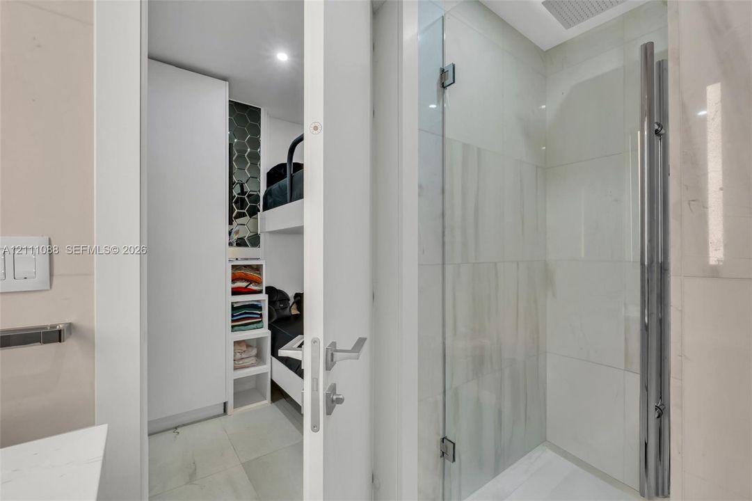 Shower enclosure featuring a seamless glass door, large-format polished wall tiling, and a vertical chrome hardware fixture