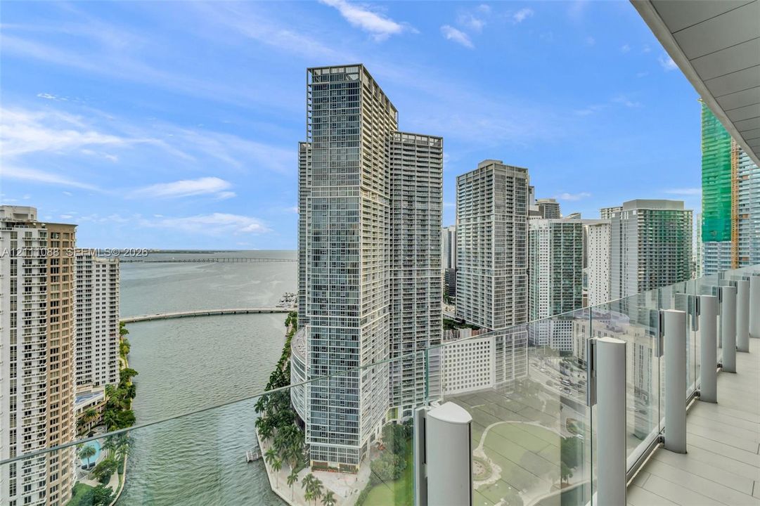 Private covered balcony with glass panel railing and tile flooring, showcasing an expansive cityscape and waterfront skyline