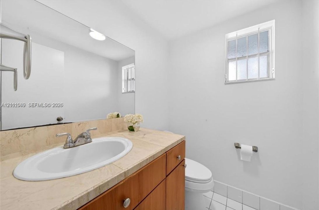 Bathroom featuring a stone-tile countertop, integrated porcelain sink, wood-finish cabinetry, large wall-mounted mirror, and a window with a grid pattern