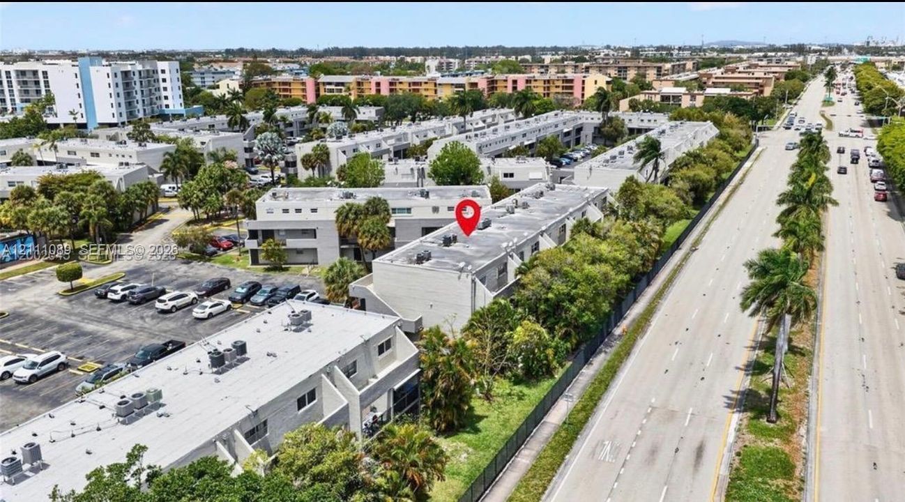 Aerial perspective featuring multi-story residential structures with flat rooflines, designated surface parking, and mature palm landscaping