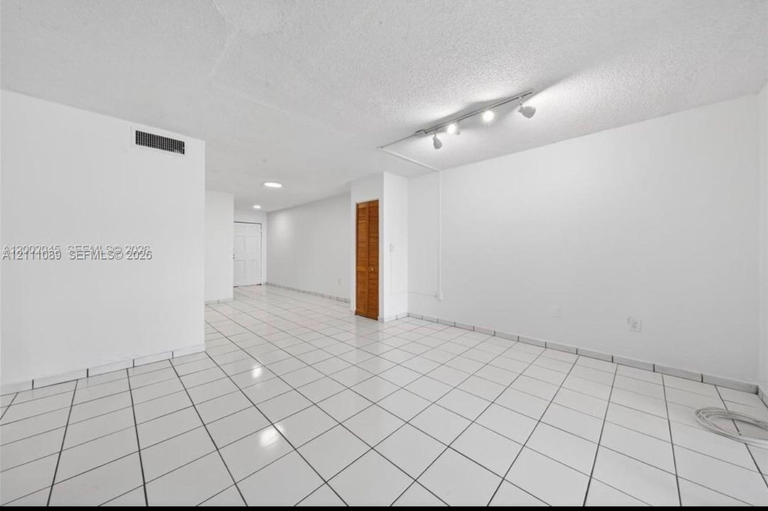 Interior space featuring white floor tiles, a textured ceiling finish, adjustable track lighting, and a bi-fold door closet
