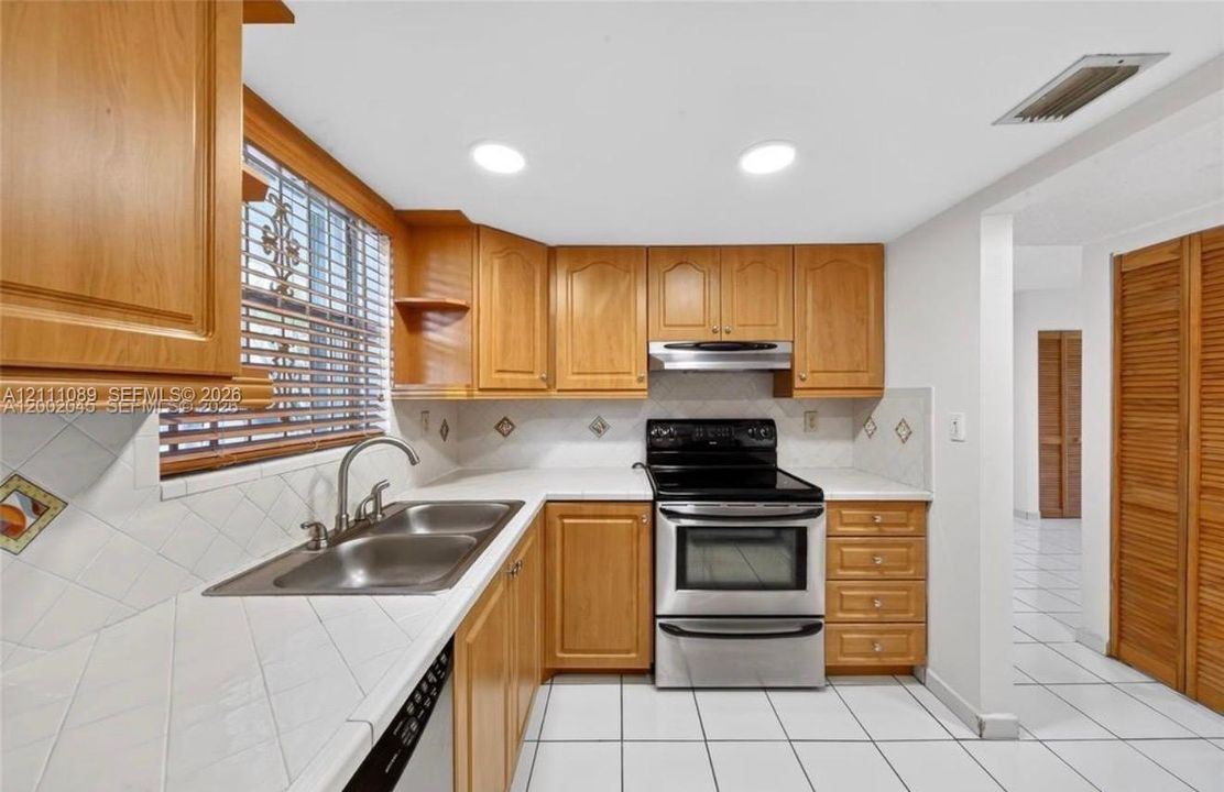 Kitchen featuring wood cabinetry, white tile countertops, stainless steel appliances, ceramic tile flooring, and recessed lighting
