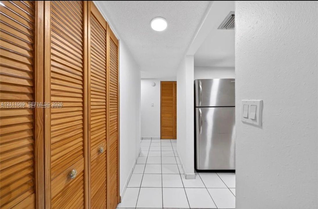 Hallway featuring wood-finish louvered closet doors, white ceramic tile flooring, and stainless steel refrigerator