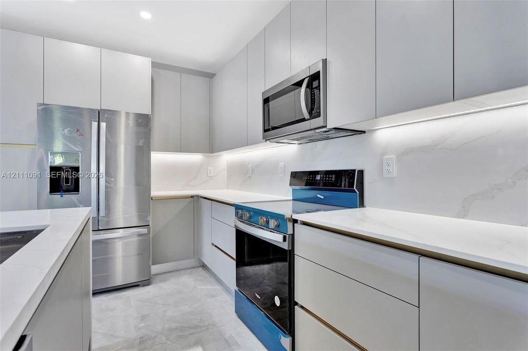 Kitchen featuring flat-panel cabinetry, stone-surface countertops, full-height stone backsplash, under-cabinet lighting, and stainless steel appliances