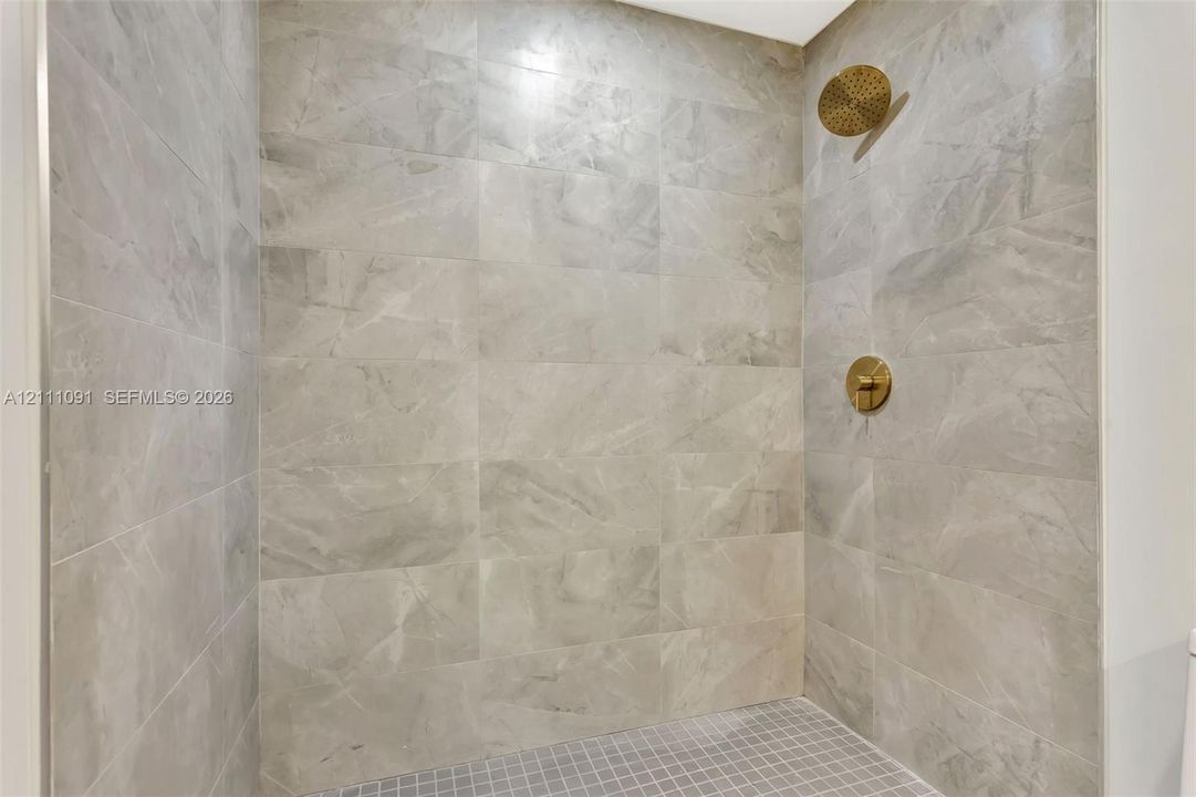 Walk-in shower featuring large-format stone-finish wall tile, a mosaic tile floor, and brushed-gold hardware including a rainfall showerhead and wall-mounted control