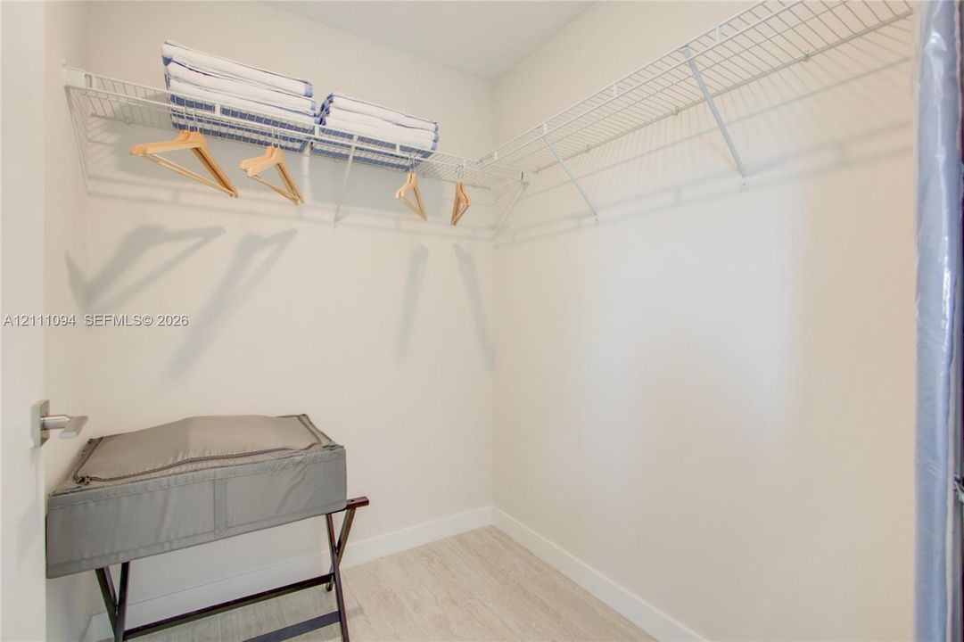 Walk-in closet featuring light-toned wood-finish flooring and dual-tier white wire shelving