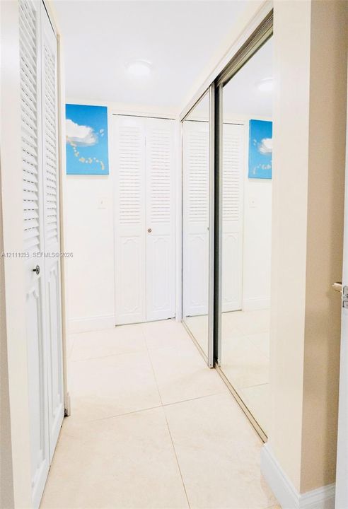 Large-format tile flooring, dual mirrored sliding closet doors, and white louvered bifold doors