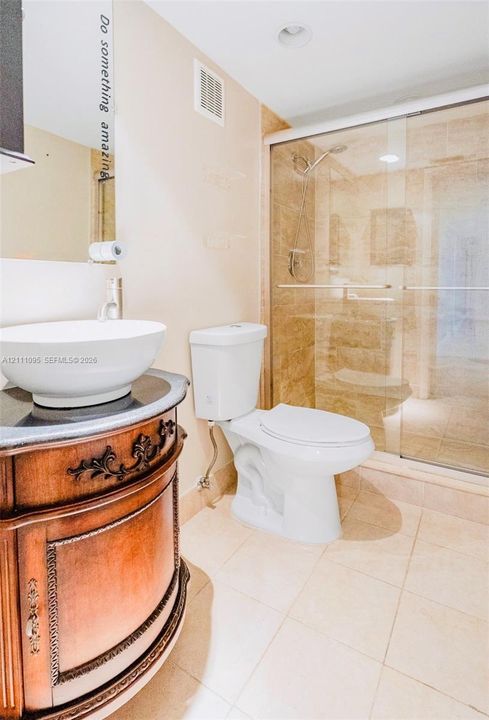 Bathroom featuring an ornate wooden vanity with a stone countertop, white vessel sink, glass-enclosed shower with tile surround, and tiled flooring