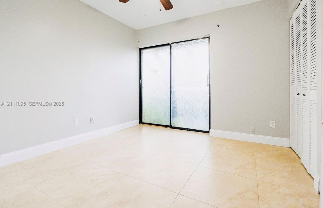 Interior space featuring oversized neutral tile flooring, sliding glass doors, white louvered-style closet doors, and a ceiling fan