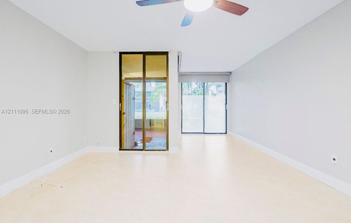 Neutral-toned interior featuring large-format tile flooring, dual sliding glass doors, and a ceiling fan with integrated lighting