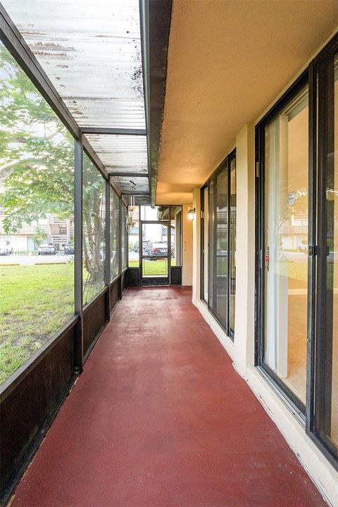 Enclosed exterior porch featuring dark metal screening, a corrugated translucent roof panel, painted concrete flooring, and sliding glass entry doors