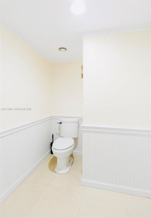 White beadboard wainscoting with chair rail molding, neutral tile flooring, and a porcelain toilet